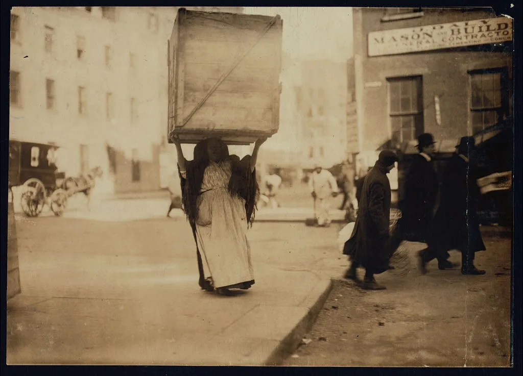 Italian woman carrying an enormous empty dry-goods-box for some…, New York (State), 1912