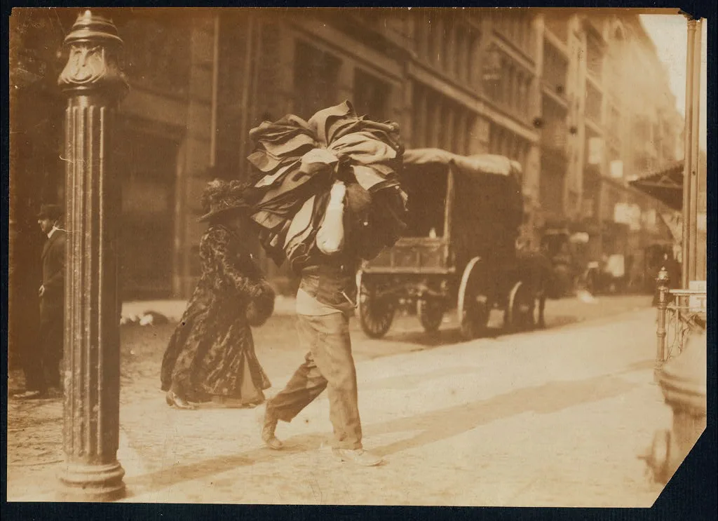 Man carrying bundle of garments. Bleecker Street, N.Y. Location: New…, New York (State), 1912